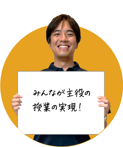 笑顔の男性が「みんなが主役の授業の実現！」と書かれたボードを持っている画像です。